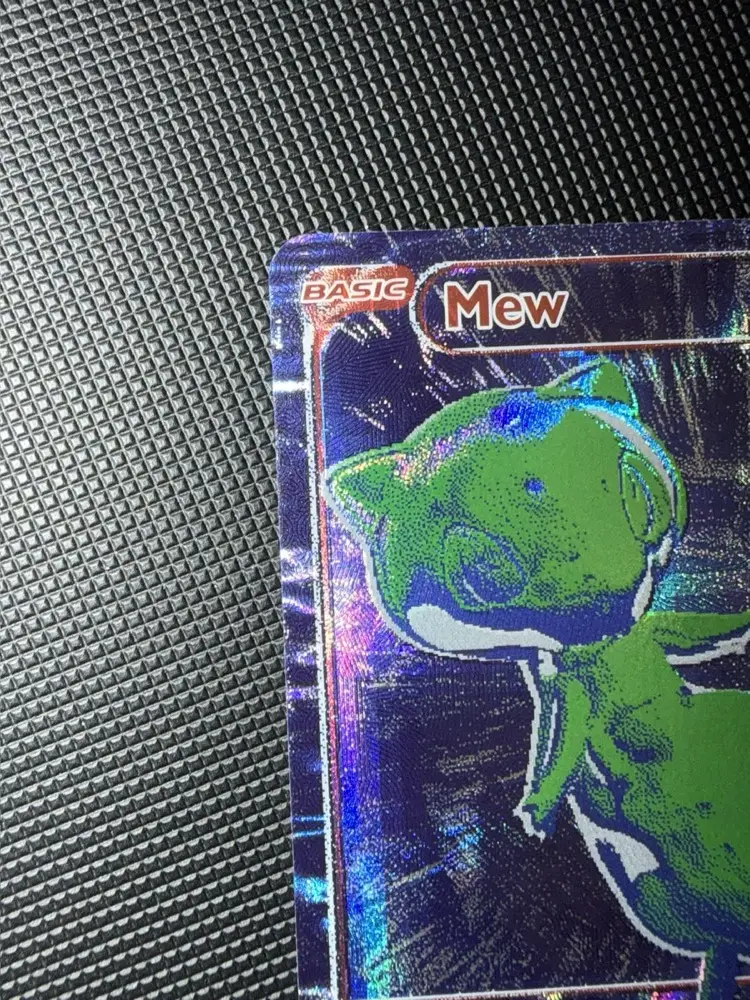 Détail du coin supérieur gauche de la carte Mew B/RGB : marqueur BASIC et nom Mew en cuivre, tête de Mew verte sur fond bleu-violet holographique
