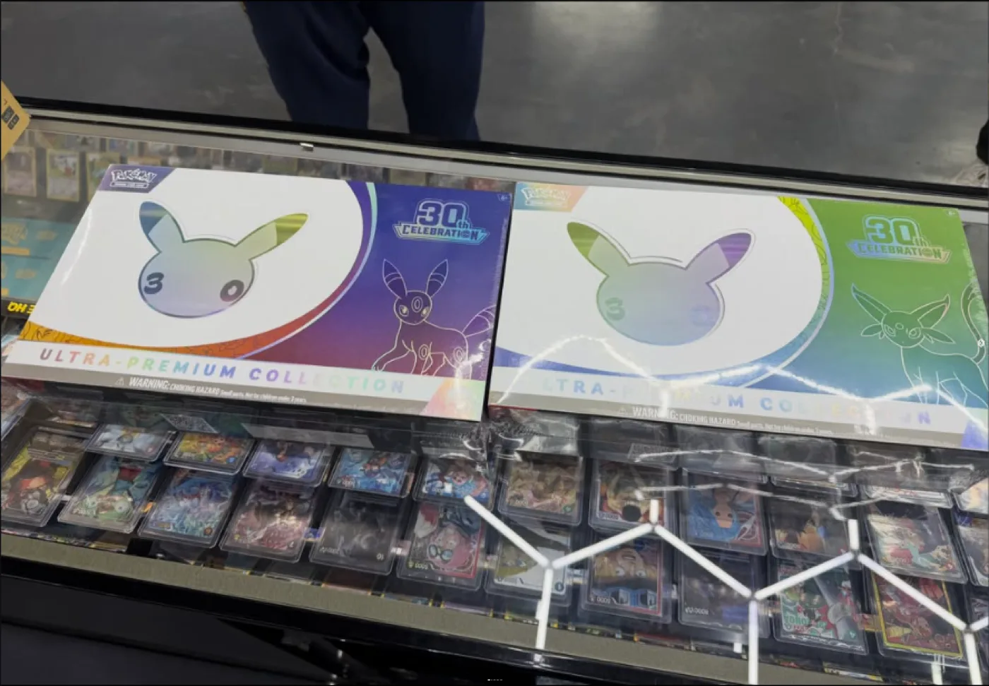 Les deux Coffrets Ultra-Premium 30th Celebration Pokémon, Journée et Soirée, posés sur une vitrine de boutique américaine avant leur sortie