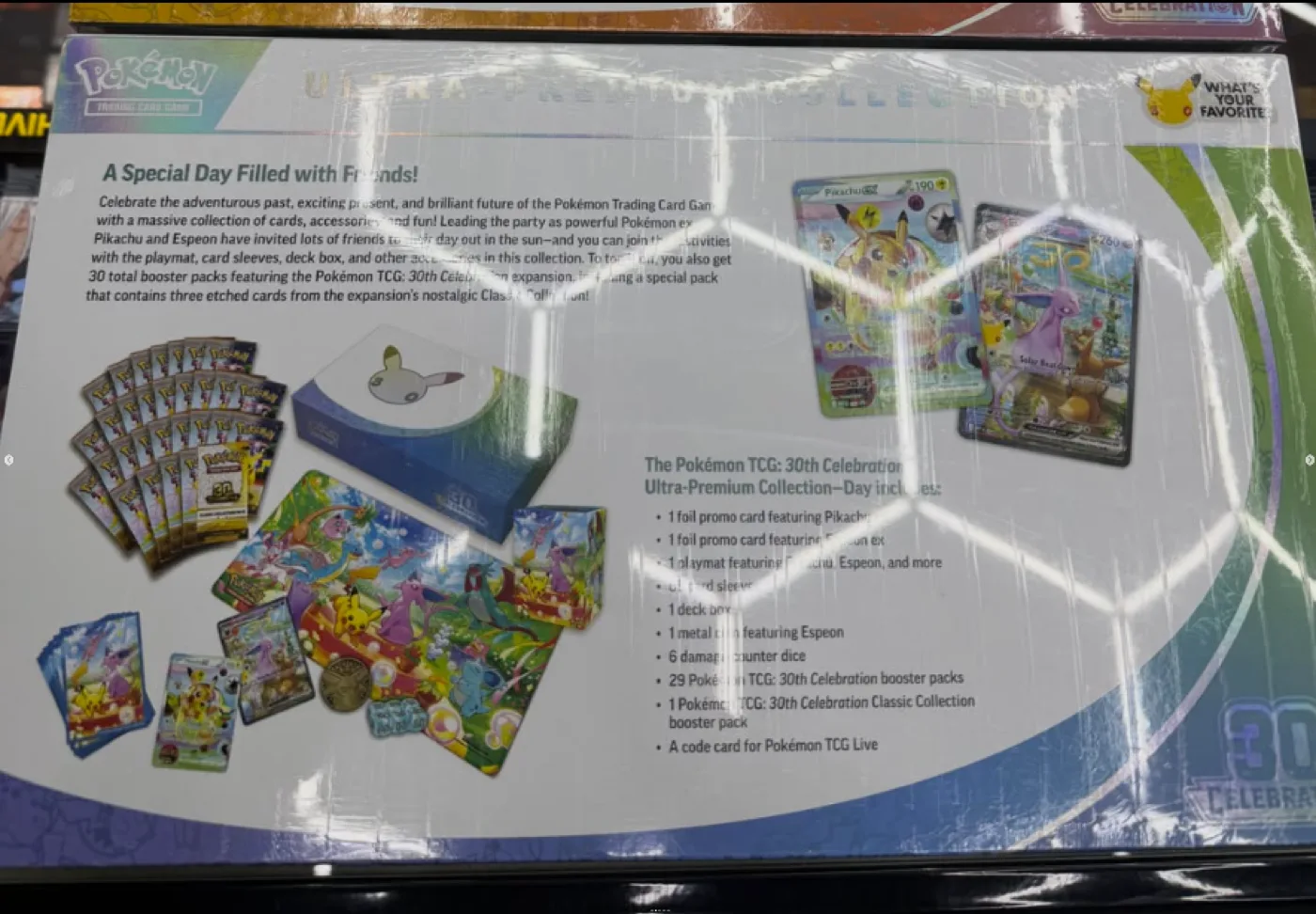 Dos de la boîte du Coffret Ultra-Premium Journée 30th Celebration listant le contenu : 29 boosters 30th Celebration, 1 booster Collection Classique, promos Pikachu ex et Espeon ex, tapis, protège-cartes, deck box, pièce en métal, 6 dés